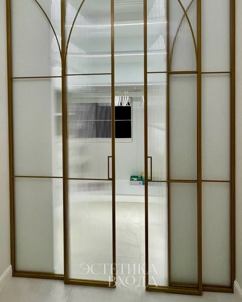 Перегородка для гардеробной комнаты с радиальным золотым профилем и вставками из рифленого стекла.
