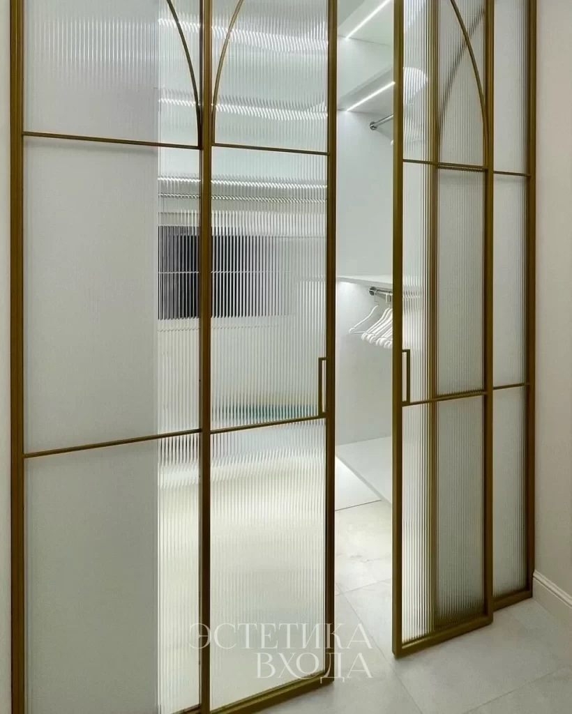 Перегородка для гардеробной комнаты с радиальным золотым профилем и вставками из рифленого стекла.